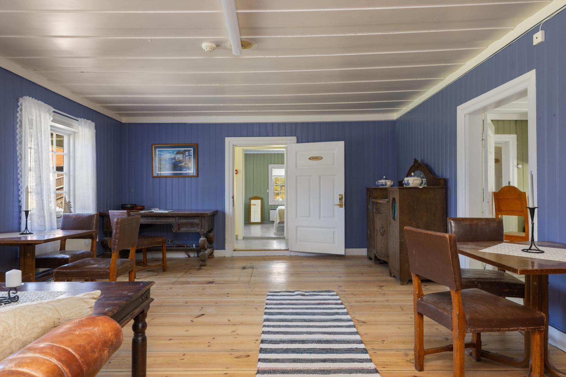 Stue i Kvitehuset med blå panelvegger, spisebord og gamle trestoler